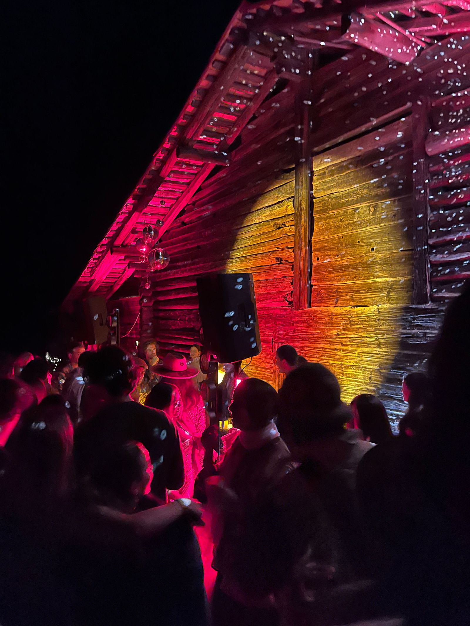 Guests outside a chalet lit in pink at night